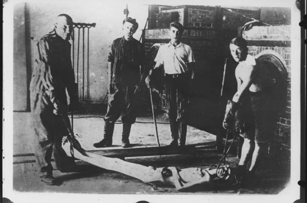 Seconda guerra mondiale - Germania - Campo di concentramento di Dachau - Nazismo - Dopo la liberazione - Crematorio, interno - Dimostrazione - Detenuti sopravvissuti con cadavere da inserire nel forno crematorio - Pinze per sollevare l'uomo