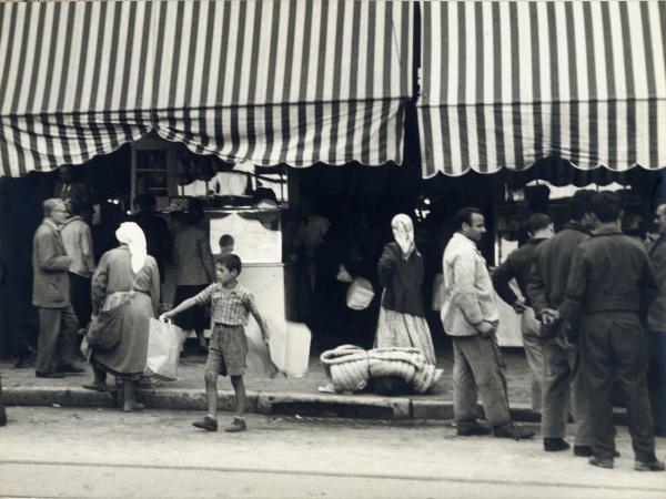 Grecia - Atene - Esterno - Strada - Mercato - Banchi con tende - Bambino con borse della spesa - Uomini e donne