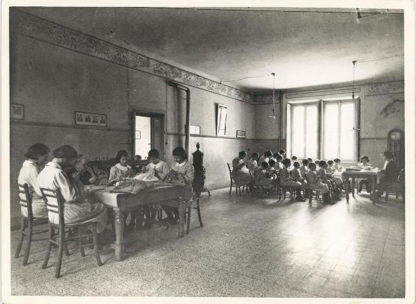 Milano - Via Monterosa - Asilo Mariuccia - Aula di lavoro - Ragazze e istitutrici cuciono - Stufa - Lampadari