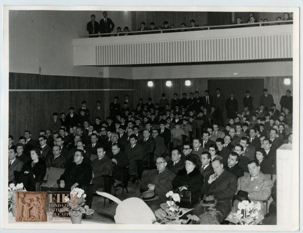 Orfanotrofio maschile di Bergamo - Bergamo - Auditorium orfanotrofio maschile: interno - Commemorazione Norberto Duzioni - Pubblico seduto: uomini e donne - Consiglieri orfanotrofio - Preti - Fiori