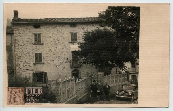 Rustici - Provincia di Bergamo - Abitazione colonica: esterno - Tre uomini e un bambino davanti all'entrata - Auto parcheggiata - Alberi