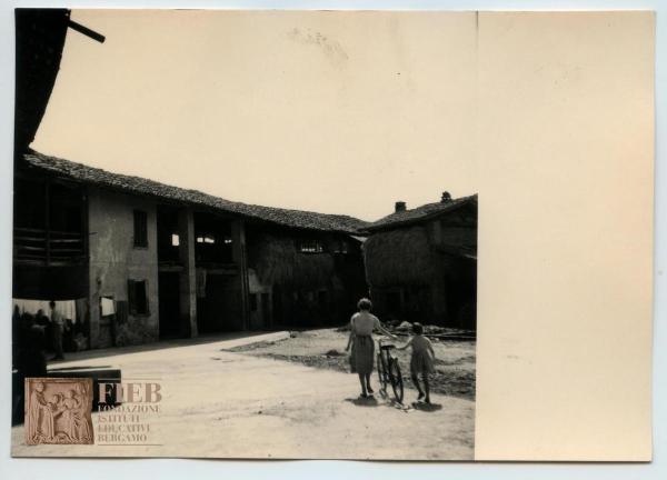 Rustici - Provincia di Bergamo - Misano - Cascina: esterno - Cortile - Una donna e una bambina spingono una bicicletta - Fieno - Panni stesi