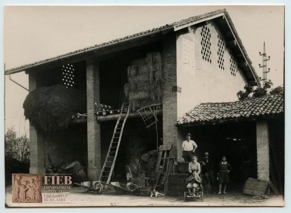 Rustici - Provincia di Bergamo - Treviglio - Castel Cerreto - Esterno cascina Fornasetta - Ritratto di gruppo: un uomo, una donna e tre giovani in posa - Cane - Fieno - Scala - Carretti