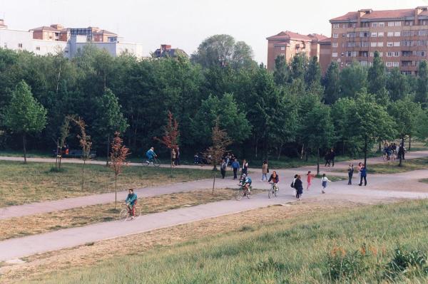 Sesto San Giovanni / Milano - Parco Nord, settore Montagnetta - Veduta dal Teatrino sull'area verso l’ingresso Suzzani - Percorsi ciclopedonali - Filari di alberi - Cannocchiale dei tigli - Persone a passeggio e in bicicletta - Festa del 25 aprile / Sullo sfondo palazzi tra viale Suzzani e viale Fulvio Testi