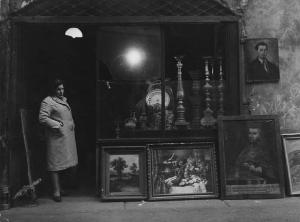 Lombardia. Milano, via Madonnina - Negozio dell'antiquariato: quadri, candelabri in vetrina - Donna sulla porta